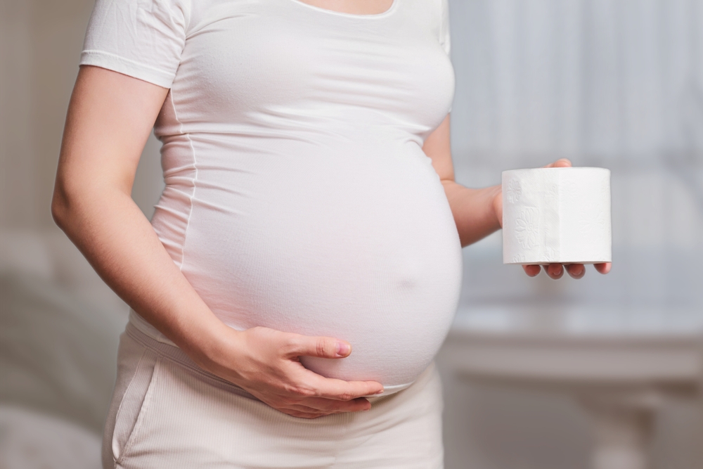 Toilet paper in the hands of a pregnant woman, studio shot, home living room